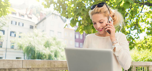 A photo of a woman answering a call on her computer in a park.